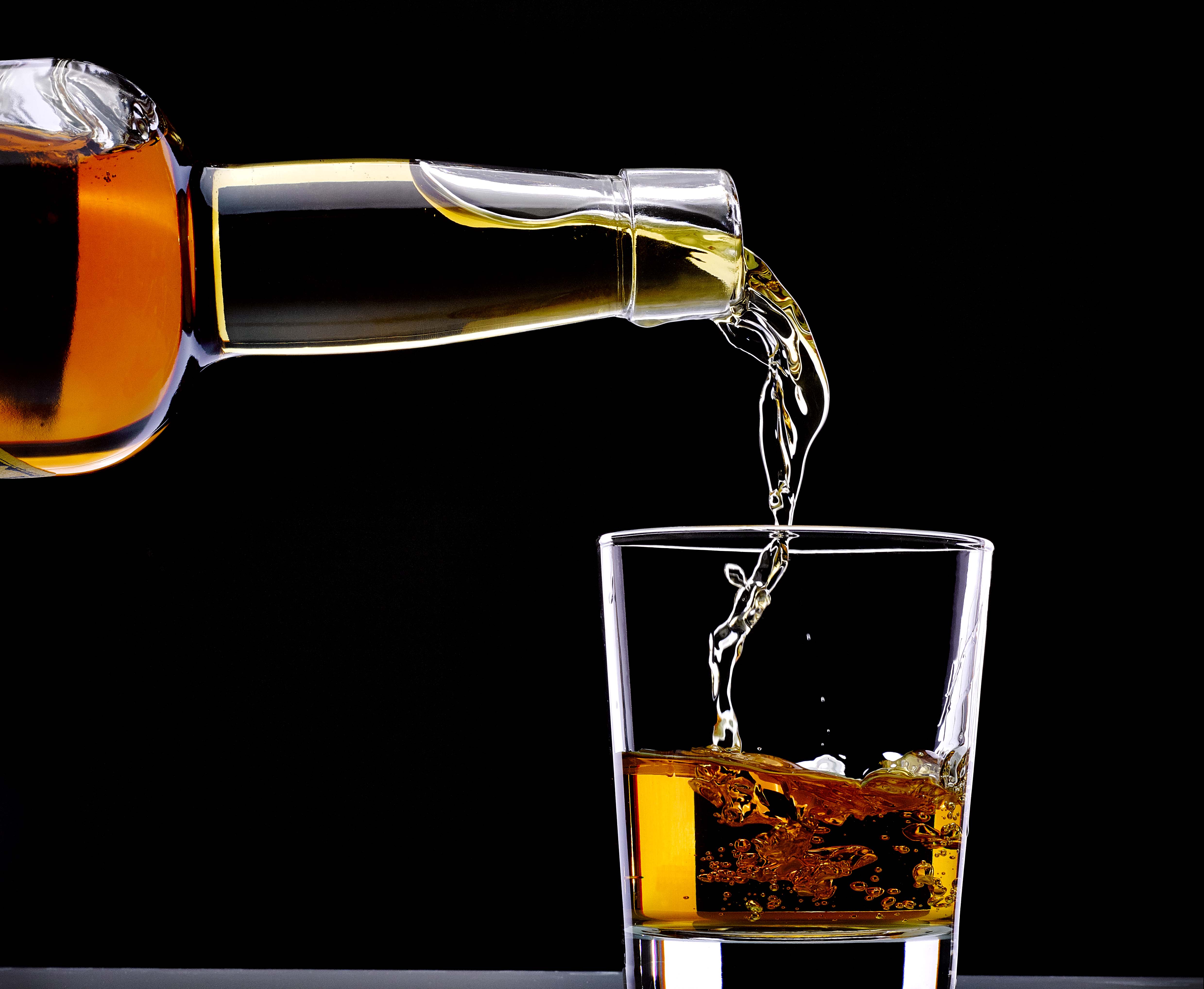 Whiskey being poured into a glass closeup on a black background